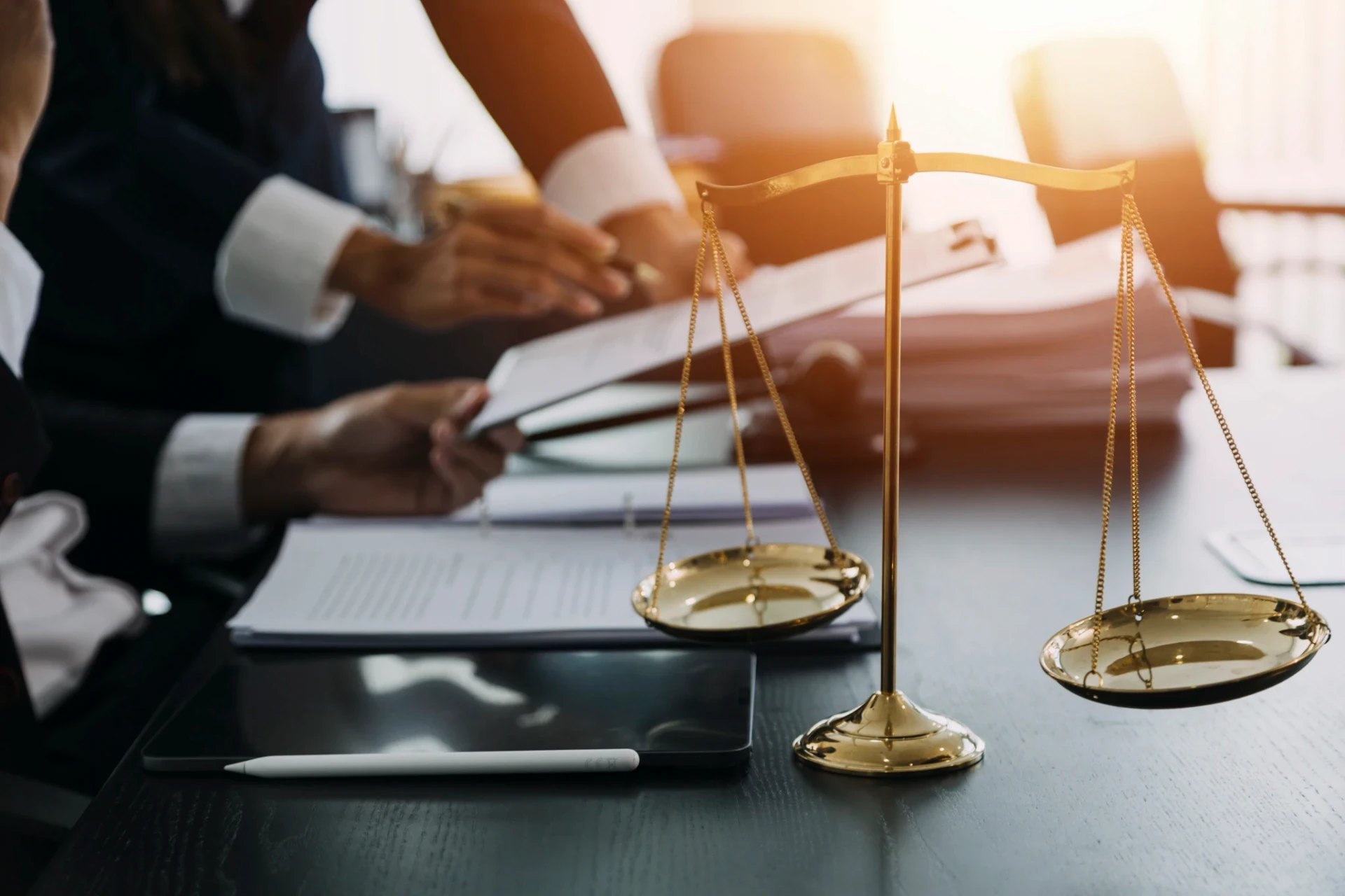Golden scales of justice on a desk beside legal documents and a tablet